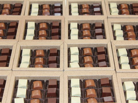 Pralinéschachteln in Reihe, bestückt mit weissen, hellen und dunklen Pralinés