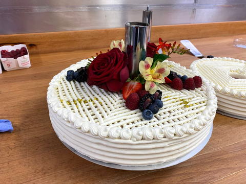 Cremetorte mit Spritzgitter, frischen Beeren und essbaren Blüten auf der Arbeitsfläche der Backstube
